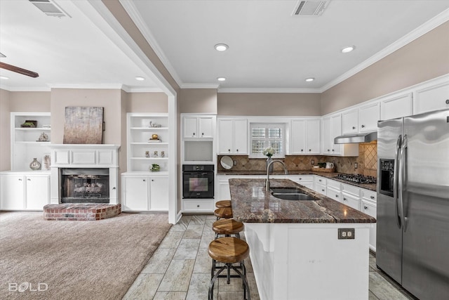 kitchen featuring an island with sink, sink, dark stone countertops, white cabinets, and stainless steel appliances