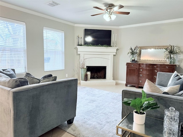 tiled living room with a brick fireplace, a ceiling fan, visible vents, and crown molding