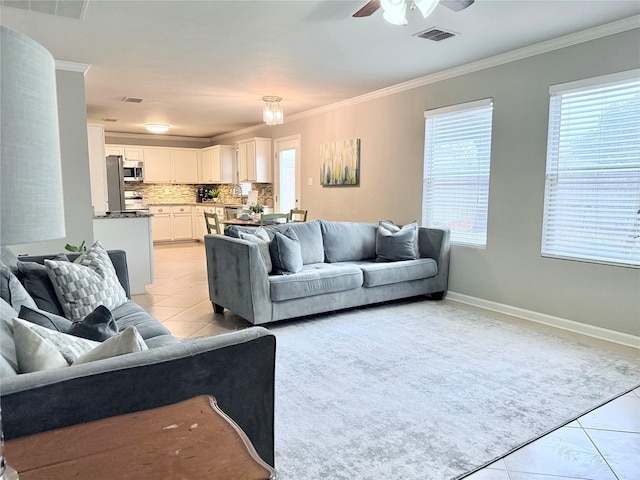 living area with light tile patterned floors, visible vents, baseboards, a ceiling fan, and ornamental molding