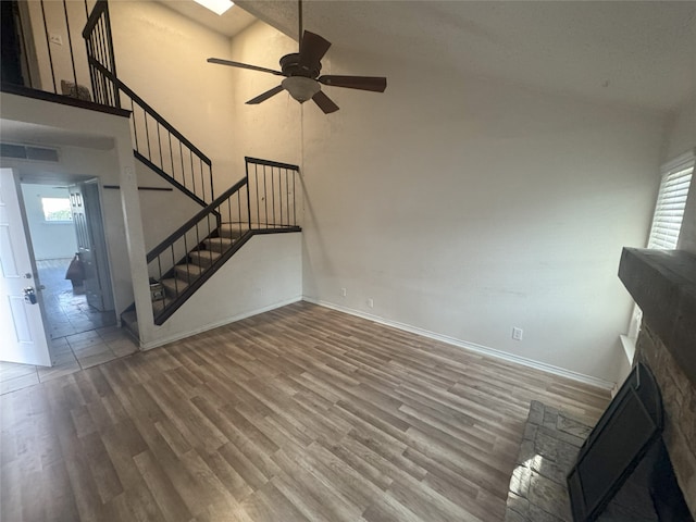 unfurnished living room featuring wood-type flooring, a stone fireplace, high vaulted ceiling, and ceiling fan