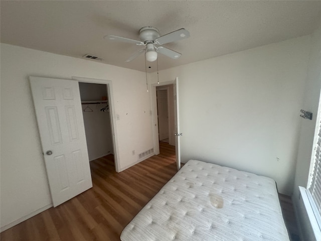 bedroom with a walk in closet, hardwood / wood-style floors, ceiling fan, and a closet