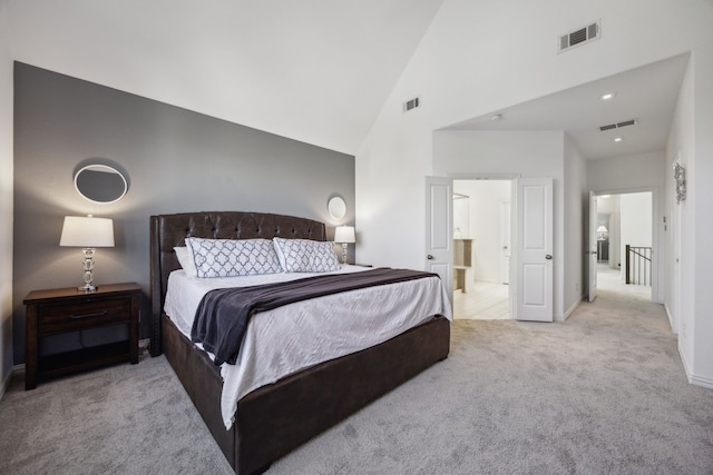 bedroom featuring light colored carpet, high vaulted ceiling, and ensuite bath