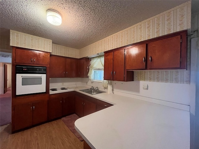 kitchen with hardwood / wood-style floors, sink, white appliances, kitchen peninsula, and a textured ceiling