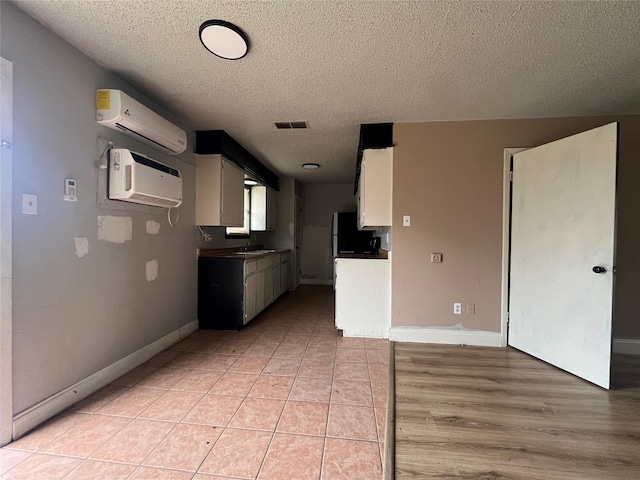 kitchen featuring white cabinetry, a wall mounted air conditioner, light tile patterned flooring, and a textured ceiling