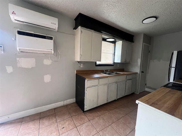 kitchen with refrigerator, a textured ceiling, white cabinets, and a wall unit AC