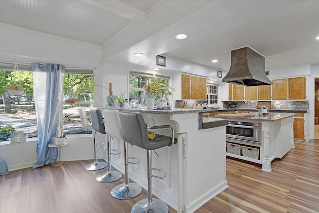 kitchen with a center island, tasteful backsplash, island range hood, stainless steel oven, and light wood-type flooring