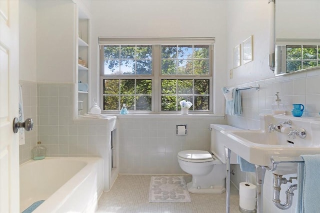 bathroom featuring a tub to relax in, tile patterned floors, toilet, and tile walls