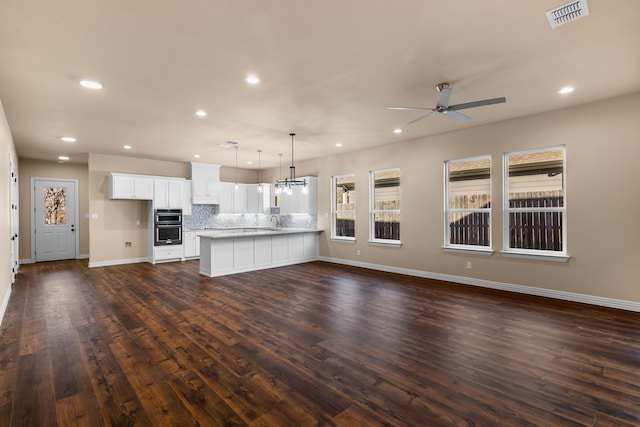 unfurnished living room with sink, ceiling fan with notable chandelier, and dark wood-type flooring