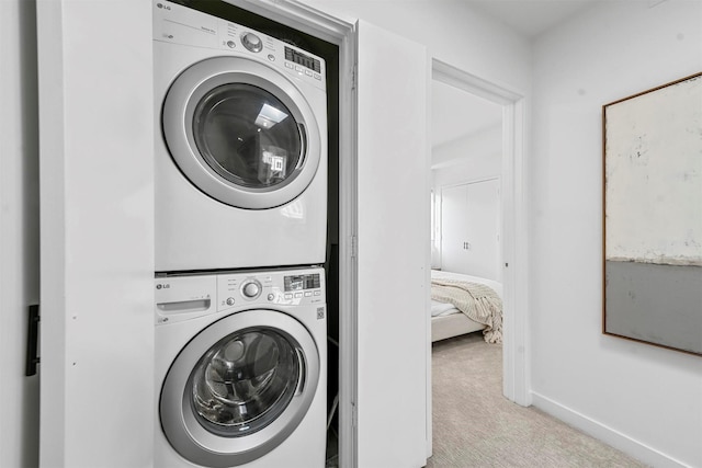 laundry room featuring stacked washer / drying machine and light colored carpet