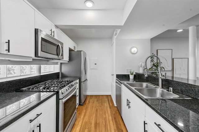 kitchen with sink, dark stone countertops, dishwasher, light hardwood / wood-style floors, and white cabinets