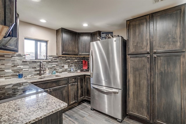 kitchen with dark brown cabinetry, sink, stovetop, light stone counters, and stainless steel fridge