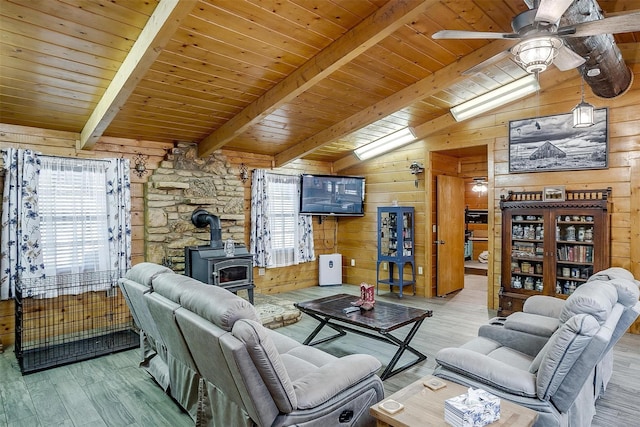 living room featuring vaulted ceiling with beams, wood ceiling, wood walls, light wood-type flooring, and a wood stove