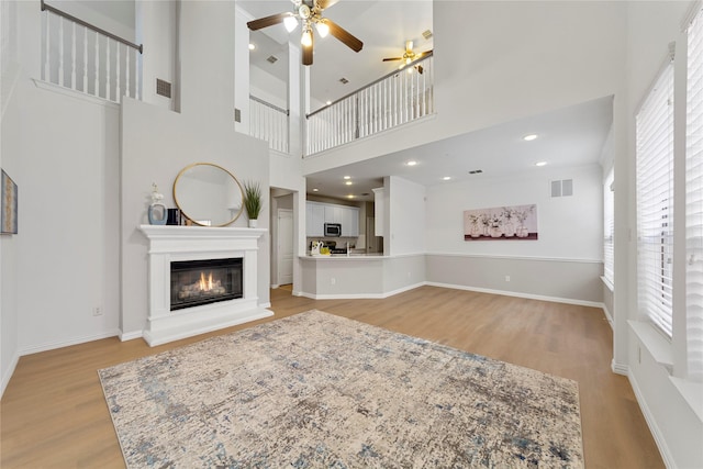 living room with a towering ceiling, light hardwood / wood-style floors, and ceiling fan