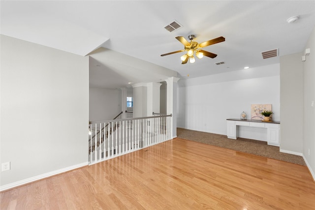 unfurnished living room with light wood-type flooring, ceiling fan, and ornate columns