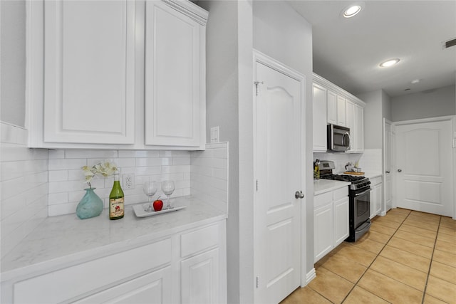 kitchen with light tile patterned flooring, appliances with stainless steel finishes, white cabinetry, decorative backsplash, and light stone countertops