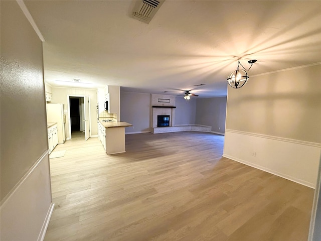 unfurnished living room featuring ceiling fan with notable chandelier, a fireplace, ornamental molding, and light wood-type flooring