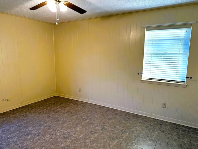 spare room featuring ceiling fan, plenty of natural light, wooden walls, and a textured ceiling