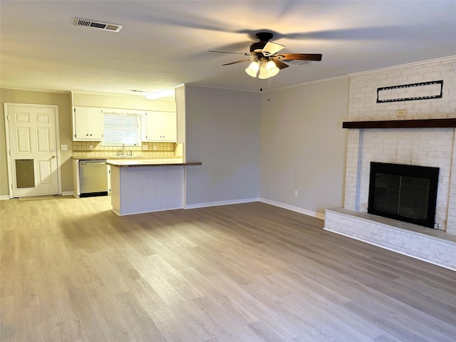 unfurnished living room featuring sink, crown molding, a brick fireplace, and light wood-type flooring