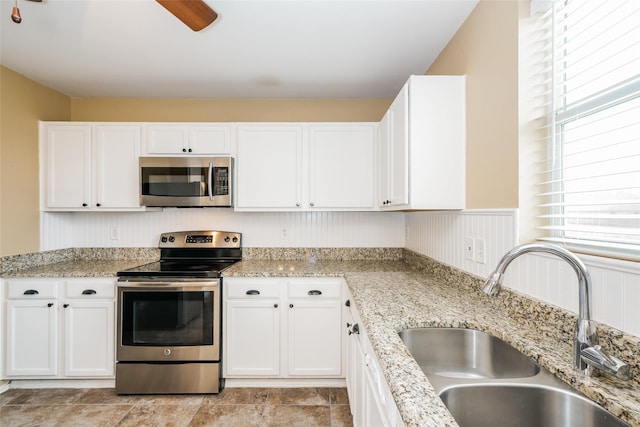 kitchen with appliances with stainless steel finishes, sink, white cabinets, ceiling fan, and light stone countertops