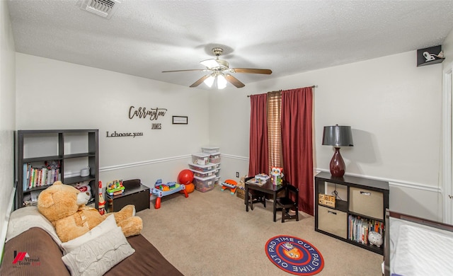 recreation room with ceiling fan, light colored carpet, and a textured ceiling