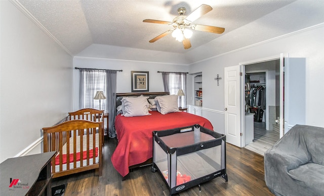 bedroom featuring dark wood-type flooring, lofted ceiling, crown molding, a walk in closet, and a textured ceiling