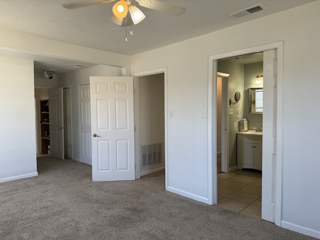 unfurnished bedroom featuring sink, ensuite bath, light colored carpet, and ceiling fan