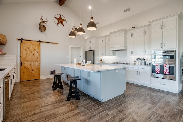 kitchen featuring white cabinetry, hanging light fixtures, beamed ceiling, stainless steel appliances, and a barn door