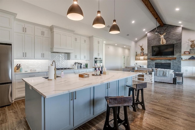 kitchen with decorative light fixtures, white cabinets, a large island with sink, light stone counters, and beam ceiling