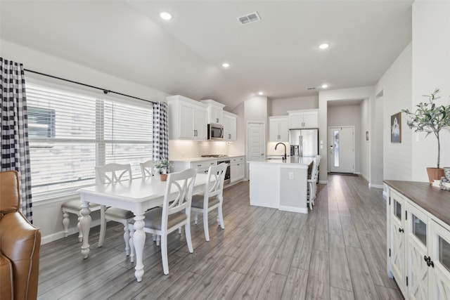 interior space featuring appliances with stainless steel finishes, a breakfast bar, white cabinets, a kitchen island with sink, and light hardwood / wood-style flooring