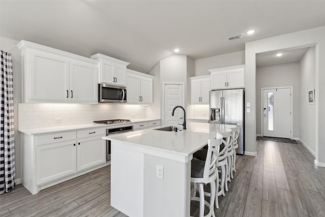 kitchen with appliances with stainless steel finishes, white cabinetry, sink, a breakfast bar area, and a center island with sink