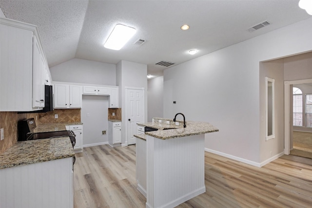 kitchen featuring vaulted ceiling, electric range oven, white cabinetry, light stone countertops, and a center island with sink