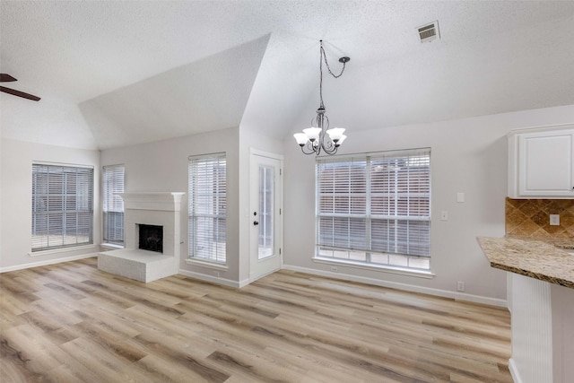 unfurnished living room with lofted ceiling, a brick fireplace, ceiling fan with notable chandelier, and light hardwood / wood-style flooring