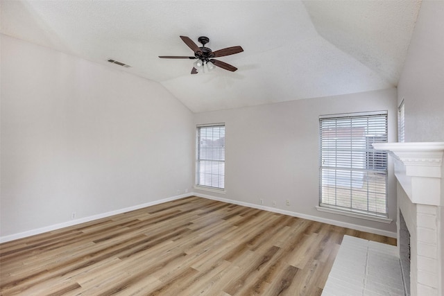 unfurnished living room featuring vaulted ceiling, a textured ceiling, light wood-type flooring, ceiling fan, and a fireplace