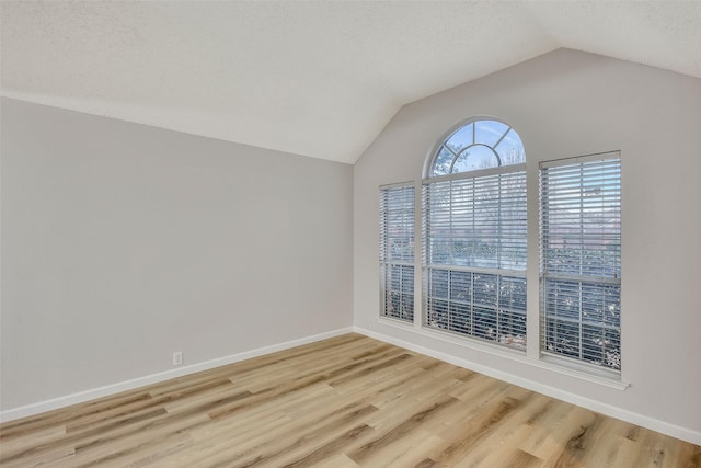 unfurnished room featuring lofted ceiling, a textured ceiling, and light hardwood / wood-style flooring