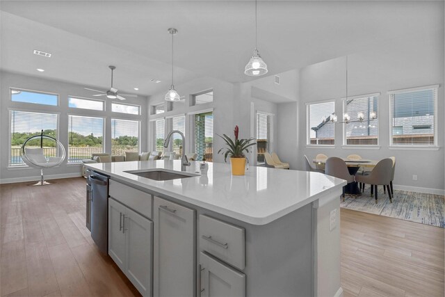 kitchen with pendant lighting, sink, light hardwood / wood-style flooring, gray cabinetry, and an island with sink