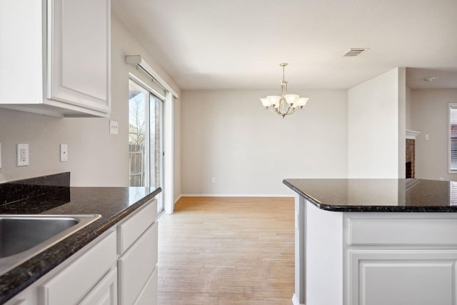 kitchen featuring white cabinets, a chandelier, dark stone counters, hanging light fixtures, and light hardwood / wood-style floors