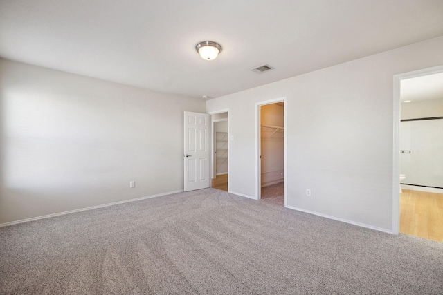 unfurnished bedroom with carpet floors, a spacious closet, ensuite bathroom, and a closet