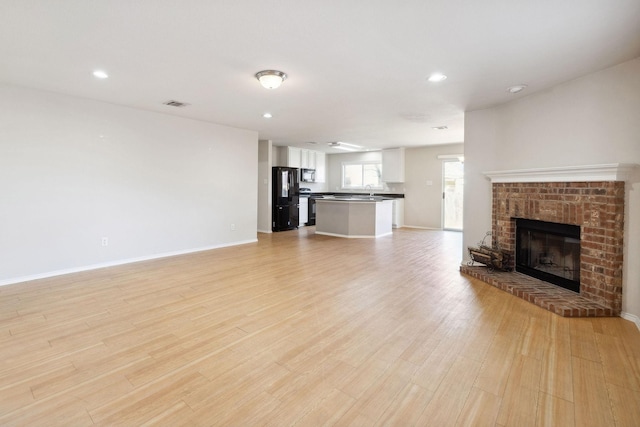 unfurnished living room with a brick fireplace and light hardwood / wood-style floors