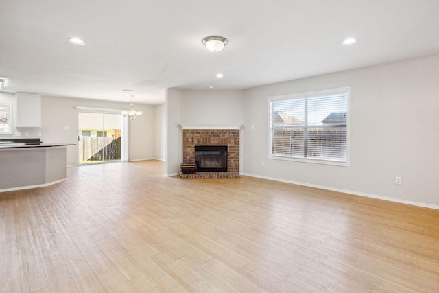 unfurnished living room with a brick fireplace, a wealth of natural light, an inviting chandelier, and light hardwood / wood-style flooring