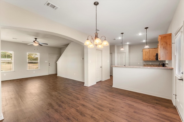 kitchen with light stone counters, hanging light fixtures, dark hardwood / wood-style floors, kitchen peninsula, and ceiling fan with notable chandelier