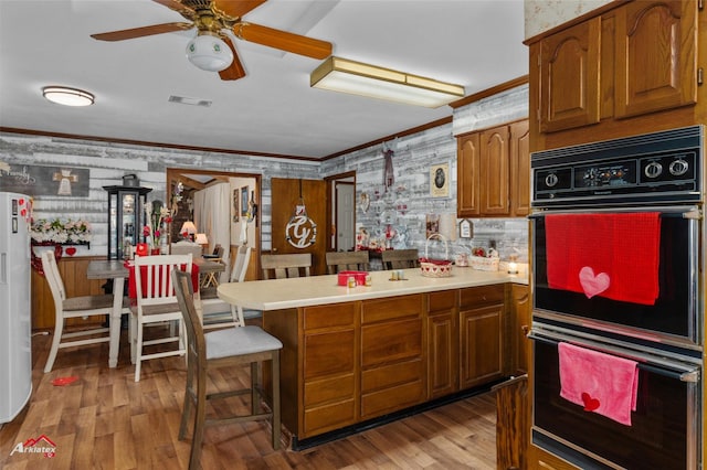 kitchen with black double oven, ornamental molding, a kitchen bar, and light hardwood / wood-style flooring