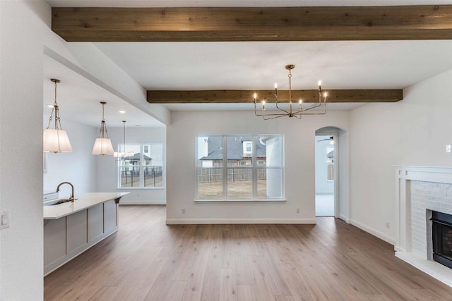 unfurnished living room with a sink, beamed ceiling, arched walkways, and a brick fireplace