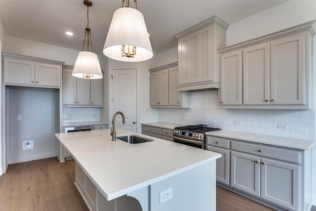 kitchen featuring light wood finished floors, a center island with sink, gray cabinets, stainless steel gas stove, and a sink