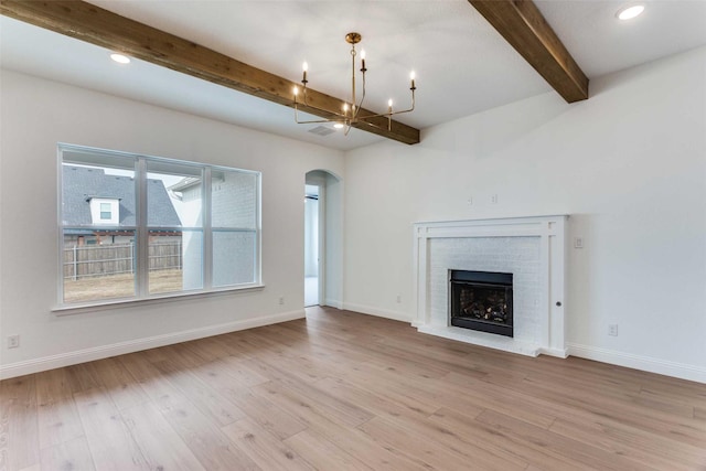 unfurnished living room with light wood-type flooring, arched walkways, a notable chandelier, and a brick fireplace