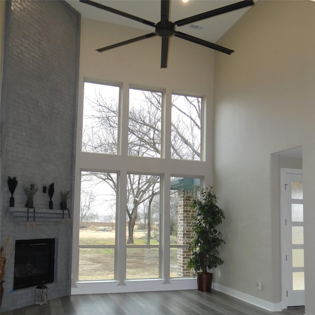 doorway to outside with ceiling fan, a towering ceiling, wood-type flooring, and a fireplace