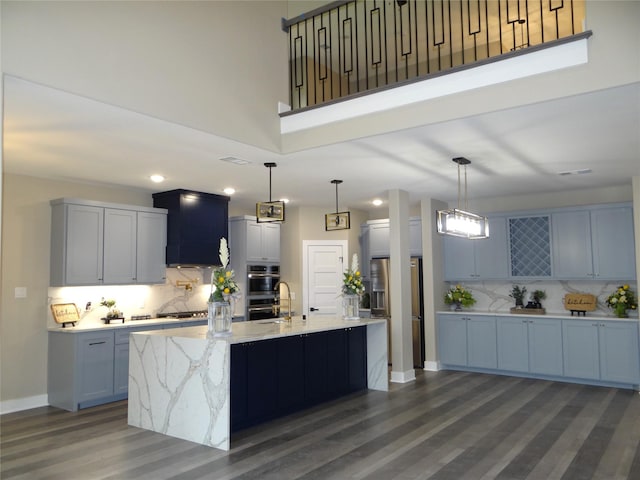 kitchen featuring light stone counters, hanging light fixtures, decorative backsplash, and an island with sink