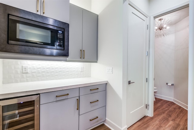 interior space with stainless steel microwave, gray cabinetry, wine cooler, backsplash, and hardwood / wood-style flooring