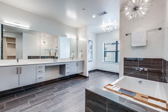 bathroom with an inviting chandelier, vanity, and a bath