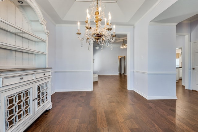 unfurnished dining area featuring a raised ceiling, crown molding, dark wood-type flooring, and ceiling fan with notable chandelier