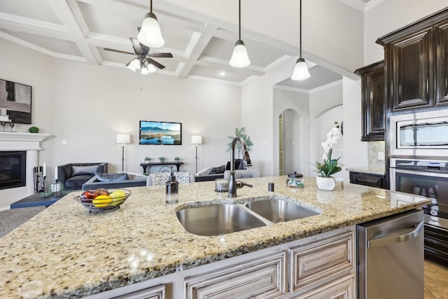 kitchen featuring pendant lighting, appliances with stainless steel finishes, open floor plan, a sink, and light stone countertops